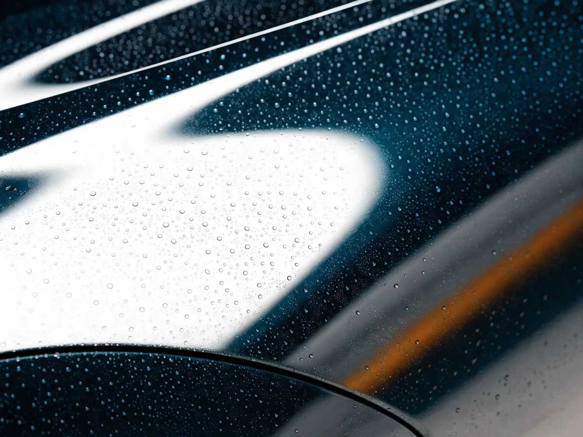 Abstrakte, markenfreie Fahrzeugoberfläche mit Wasserperlen und kontrollierter Lichtreflexion